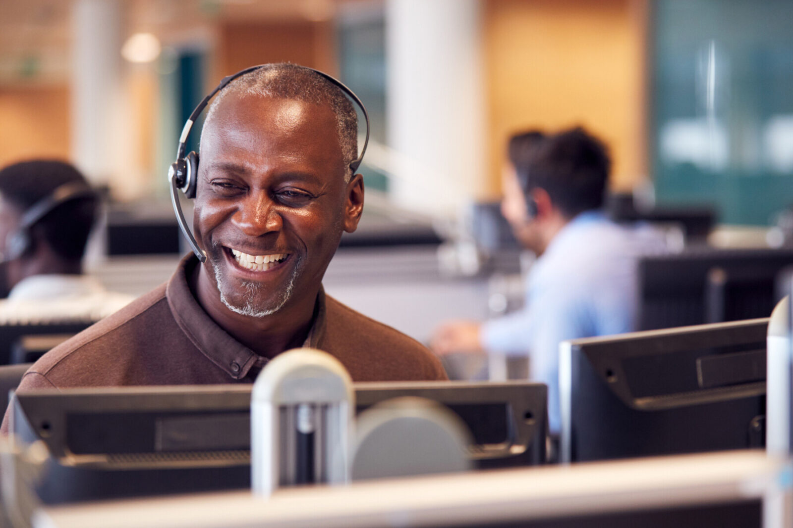 Mature Businessman Wearing Telephone Headset Talking To Caller In Customer Services Department