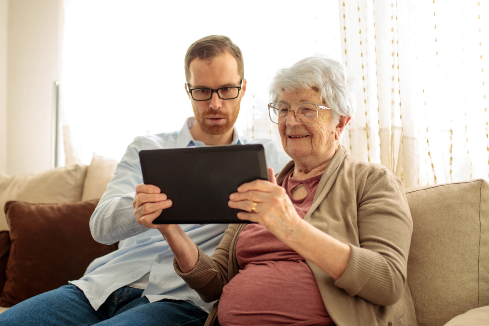 Young man teaching his grandmother how to use a tablet