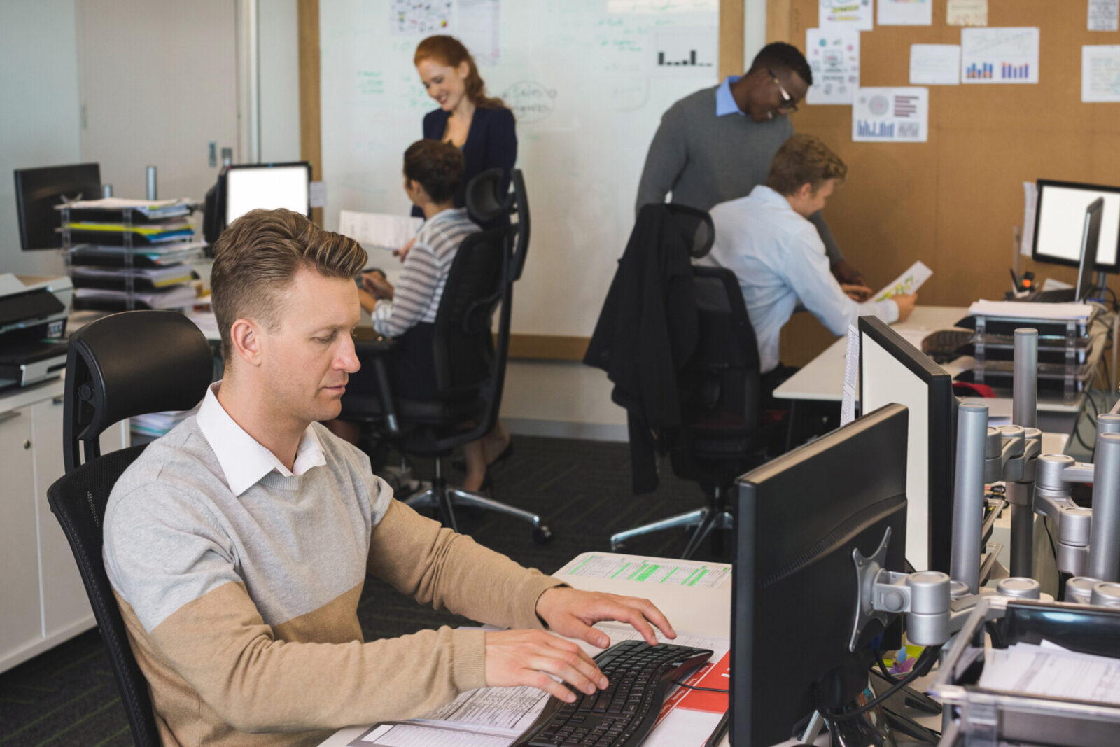 Businessman typing on keyboard while colleagues working in background