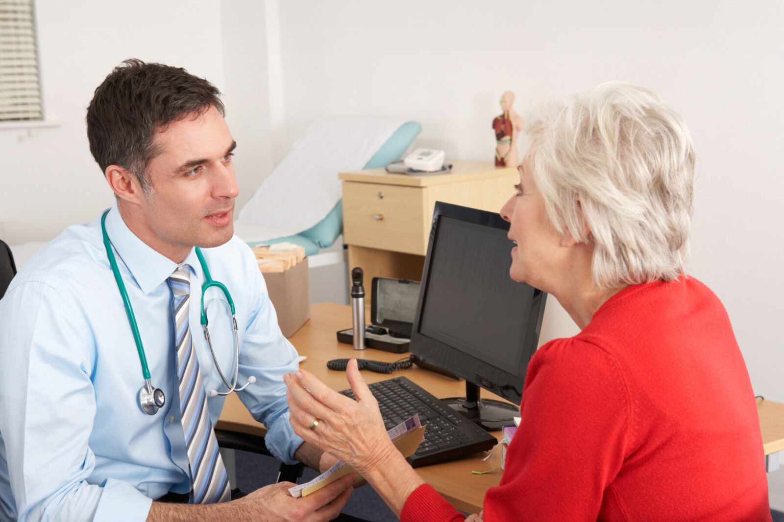 British GP talking to senior woman in surgery